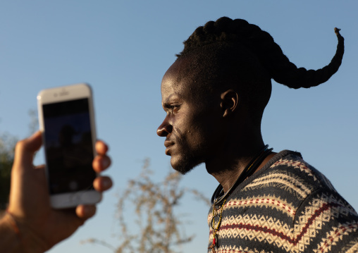 Tourist taking a picture with a mobile phone of a himba tribe single man, Cunene Province, Oncocua, Angola