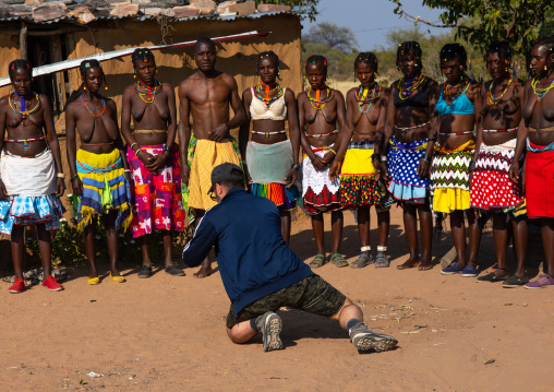 European tourist filming mudimba tribe women in traditional clothing, Cunene Province, Cahama, Angola