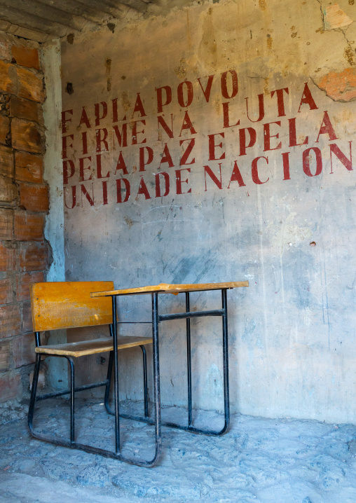 School desk in a classroom with old propaganda on the wall about forcas armadas populares de libertacao de angola popular armed, Cunene Province, Cahama, Angola
