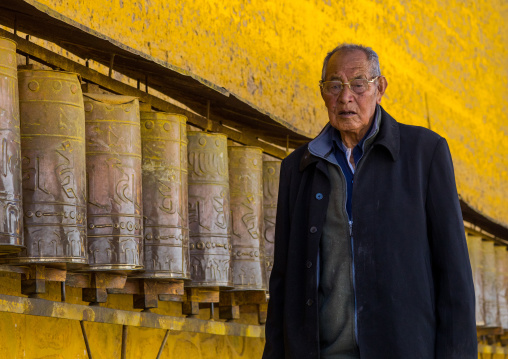 Tibetan pilgrim man turning huge prayer wheels in Rongwo monastery, Tongren County, Longwu, China