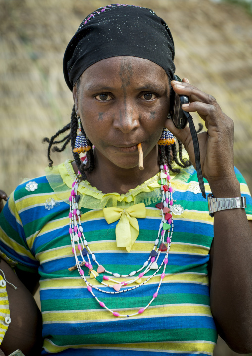 Benin, West Africa, Gossoue, a beautiful tattooed fulani peul tribe woman pausing with her mobile phone
