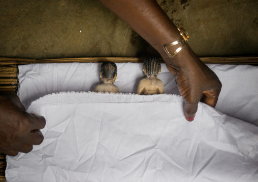 Benin, West Africa, Bopa, miss hounyoga putting the carved wooden figures made to house the soul of her dead twins in a bed