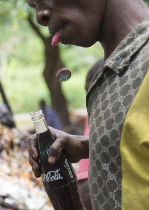 Benin, West Africa, Dankoly, a man opening with his teeth a coca cola bottle during a voodoo ceremony