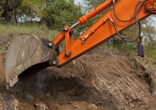 Indigenous Woman And Mechanical Digger Arm On Coated Road  Construction Work In Mago Park Omo Valley Ethiopia