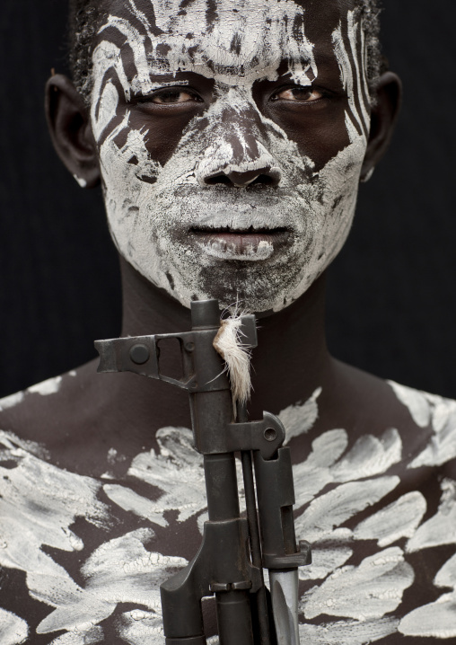 Portrait Of Painted Face Karo Young Man With White Paint And Kalashnikov Rifle Barrel  Omo Valley Ethiopia