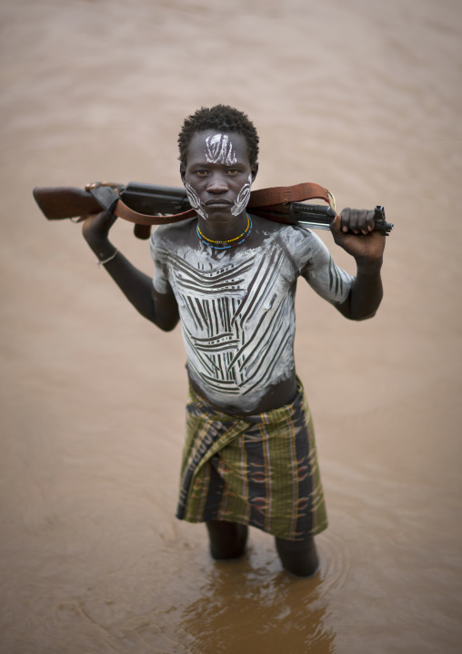 Young Karo Man With White Painted Faces And Chests Holding Kalashnikov Rifle In The Water Of The River Omo Valley Ethiopia