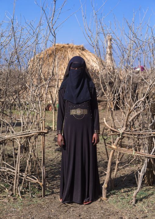 An ethiopian oromo woman dressed in black burqa stands in front of her hut, Amhara region, Artuma, Ethiopia