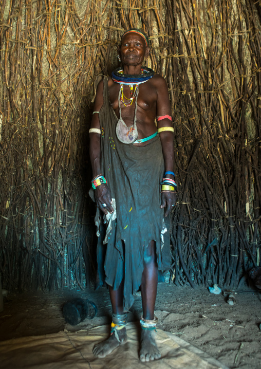 Toposa tribe woman with an animal skin skirt standing in her hut, Omo valley, Kangate, Ethiopia