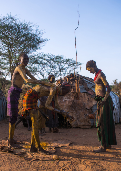 A dassanech man puts some mud on his friend body to join the dimi ceremony, Omo valley, Omorate, Ethiopia