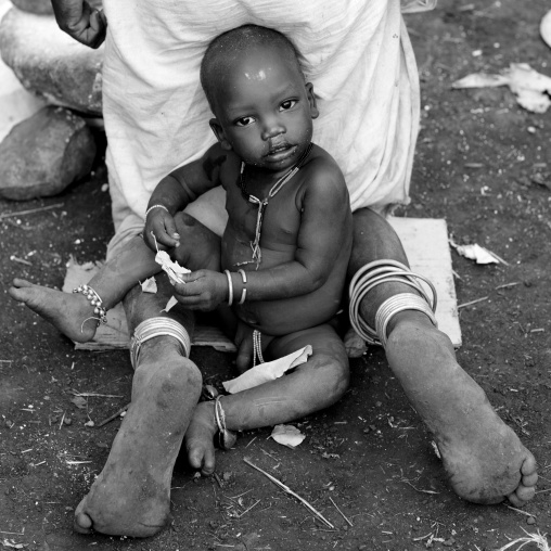 Young Suri Boy Sitting Between His Mother S Feet, Turgit Village, Omo Valley, Ethiopia