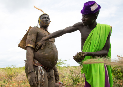 A man covers a Bodi tribe fat man with cow dungs during Kael ceremony, Omo valley, Hana Mursi, Ethiopia