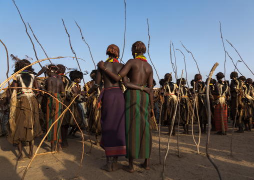 Girls looking at Dassanech men with leopard skins and ostrich feathers wigs during Dimi ceremony to celebrate circumcision of teenagers, Turkana County, Omorate, Ethiopia