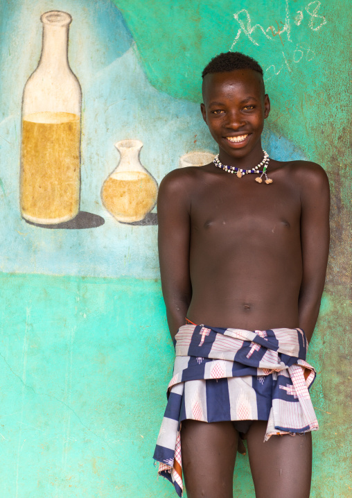 Young Bana tribe boy in front of a painted mural for tej drink in a bar, Omo valley, Key Afer, Ethiopia