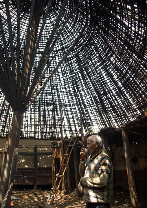 Old man drinking a coffee under a Gurage traditional roof without thatch in renovation, Gurage Zone, Butajira, Ethiopia