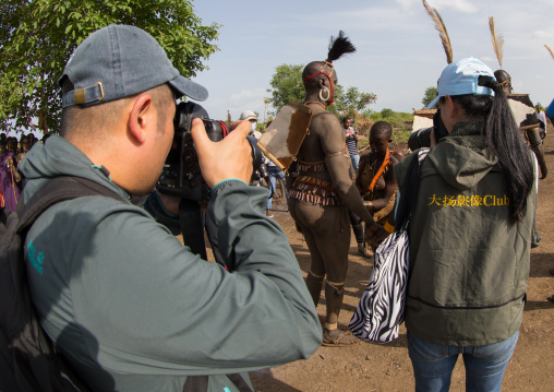 Chinese tourists taking pictures of Bodi tribe fat men during Kael ceremony, Omo valley, Hana Mursi, Ethiopia