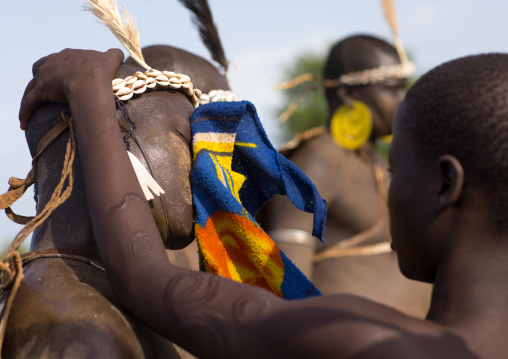 Woman wiping the sweat of a Bodi tribe fat man during Kael ceremony, Omo valley, Hana Mursi, Ethiopia
