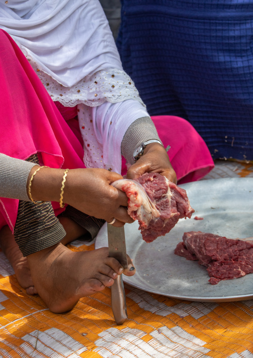 Harari woman cutting meat with a knife she holds with her foot, Harari Region, Harar, Ethiopia