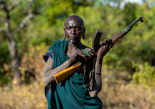 Suri tribe warrior with a kalashnikov spitting, Omo valley, Kibish, Ethiopia
