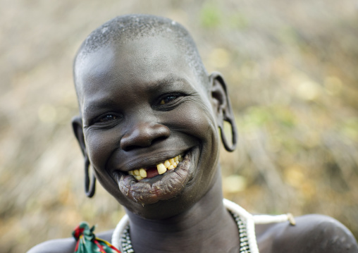 Portrait of a surma tribe woman with enlarged lip and ears and toothy smile, Tulgit, Omo valley, Ethiopia