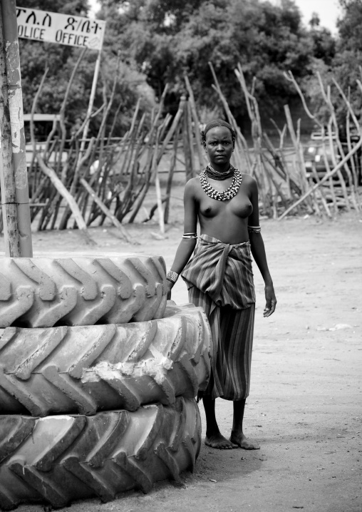 Black and white portrait of a young dassanech tribe girl next to truck tires, Omorate, Omo valley, Ethiopia