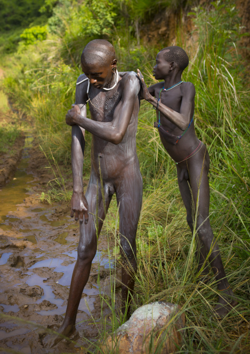 Shepherd from Suri tribe receiving help to decorate his body with camouflage paintings, Tulgit, Omo valley, Ethiopia