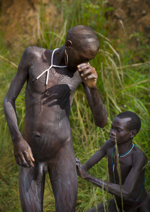 Shepherd from Suri tribe receiving help to decorate his body with camouflage paintings, Tulgit, Omo valley, Ethiopia