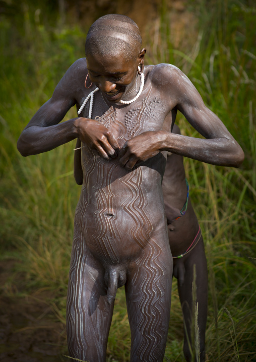 Shepherd from Suri tribe receiving help to decorate his body with camouflage paintings, Tulgit, Omo valley, Ethiopia