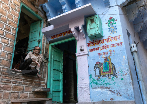 Indian man squatting near an old blue house of a brahmin, Rajasthan, Jodhpur, India