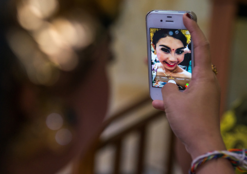 A Teenager Girl In Traditional  Costume Using Her Mobile Phone As A Mirror  Before A Tooth Filing Ceremony