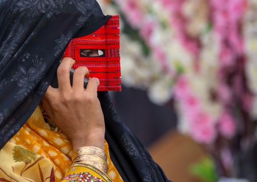 a bandari woman wearing a traditional mask called the burqa calling on a mobile phone, Hormozgan, Minab, Iran