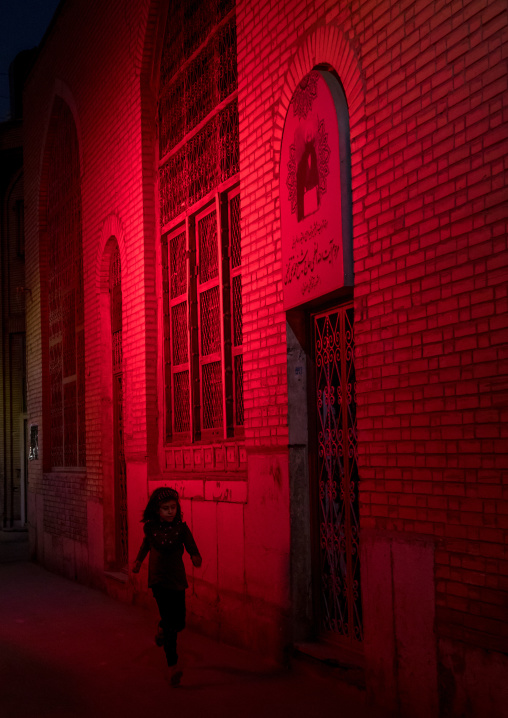 Iranian girl running in a street illuminated with red light for Muharram to commemorate the martyrdom anniversary of Hussein, Isfahan Province, Isfahan, Iran
