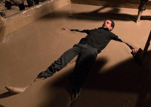 An iranian shiite muslim man rolls lies in a mud pond as he takes part in the Kharrah Mali ritual during the Ashura ceremony, Lorestan Province, Khorramabad, Iran
