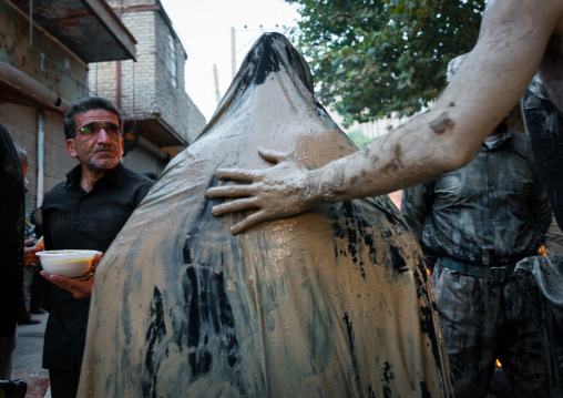 Iranian shiite muslim man leading a woman covered with mud during the Kharrah Mali ritual to mark the Ashura day, Lorestan Province, Khorramabad, Iran
