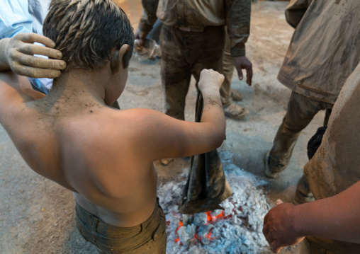 Iranian shiite child drying his clothes around a bonfire after rubbing mud on his body during the Kharrah Mali ritual to mark the Ashura day, Lorestan Province, Khorramabad, Iran