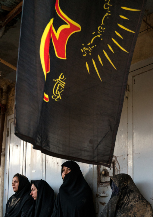 Iranian shiite muslims women standing under a giant flag after rubbing mud on their chadors during the Kharrah Mali ritual to mark the Ashura ceremony, Lorestan Province, Khorramabad, Iran