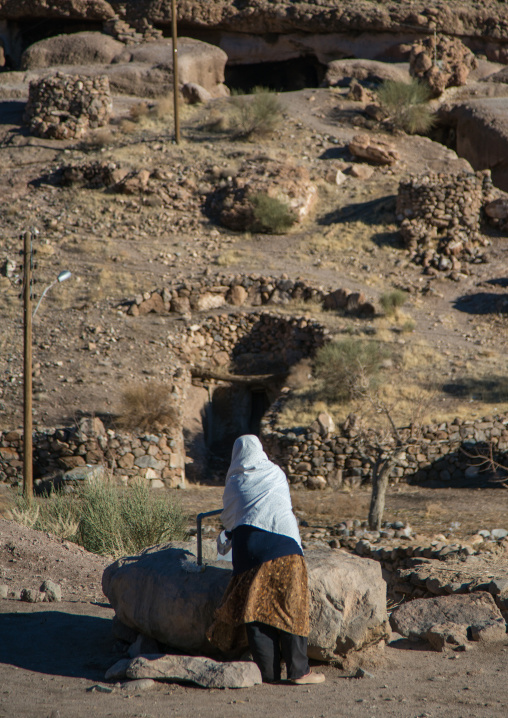 old widow woman collecting water at a well in the troglodyte village, Kerman province, Meymand, Iran