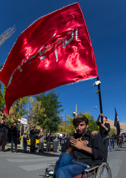 Man In Wheelchair In Front Of A Red Flag Celebrating Ashura, The Day Of The Death Of Imam Hussein, Kurdistan Province, Bijar, Iran