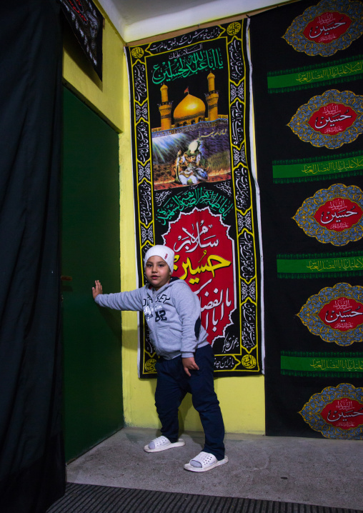 Iranian Shiite Child Closing A Door Where Stand People Waiting To Collect Nazri Charity Food During Muharram, Golestan Province, Gorgan, Iran