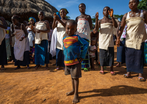 Boy with a Superman shirt in front of dan tribe women singing and dancing during a ceremony, Bafing, Gboni, Ivory Coast