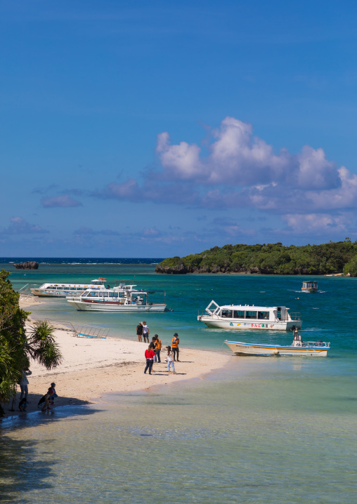 Glass bottom boats in the tropical lagoon beach with clear blue water and white sand surrounded by lush greenery in Kabira bay, Yaeyama Islands, Ishigaki, Japan