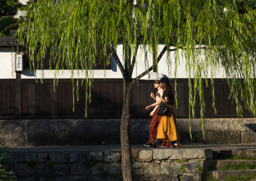 Japanese women with an umbrella passing in front old houses along the riverbank, Okayama Prefecture, Kurashiki, Japan