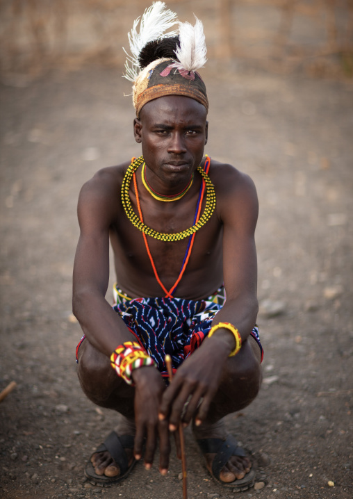 Portrait of a Turkana tribe man squatting with ostrich feathers on the headwear, Rift Valley Province, Turkana lake, Kenya