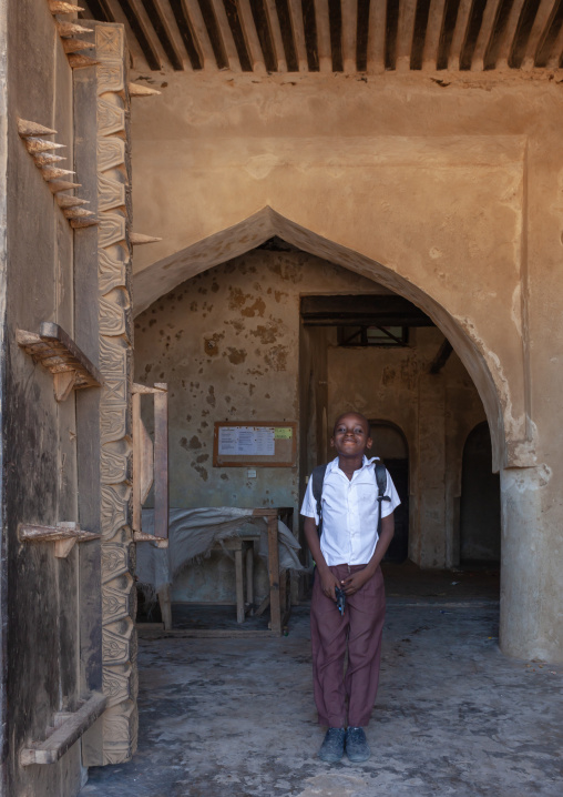Kenyan pupil standing in front of a arved wooden front door, Lamu County, Lamu, Kenya
