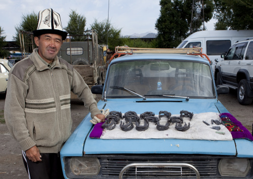 Man With Kalpak Hat Selling Horseshoes On His Car S Bonnet, Animal Market Of Kochkor, Kyrgyzstan