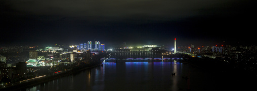 New modern buildings illuminated at night in front of the Juche tower, Pyongan Province, Pyongyang, North Korea