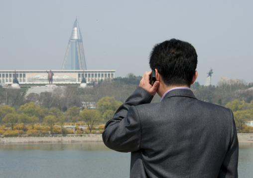 North Korean man calling with his mobile in front of the pyramid-shaped Ryugyong hotel, Pyongan Province, Pyongyang, North Korea