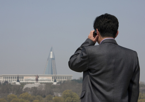 North Korean man calling with his mobile in front of the pyramid-shaped Ryugyong hotel, Pyongan Province, Pyongyang, North Korea