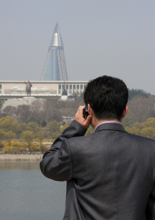 North Korean man calling with his mobile in front of the pyramid-shaped Ryugyong hotel, Pyongan Province, Pyongyang, North Korea