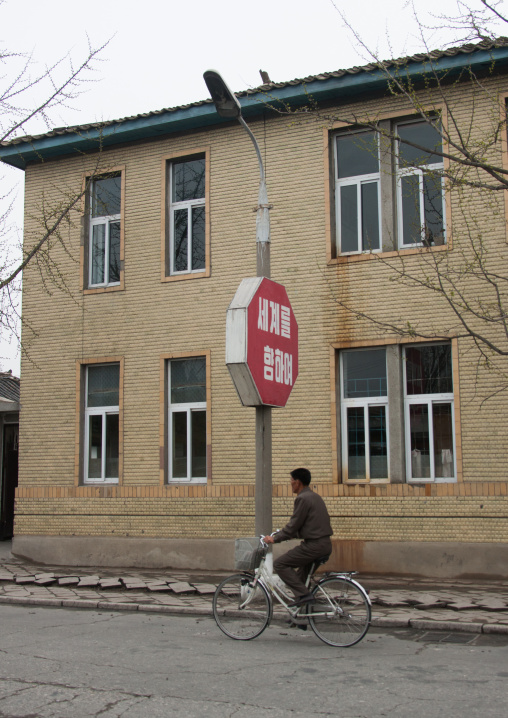 North Korean man on a bicycle passing in front of a propaganda sign, North Hwanghae Province, Kaesong, North Korea