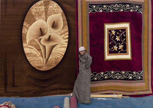 Smiling Man Standing In Front Of Two Wall Hanging Carpets, Ibra Souq, Oman